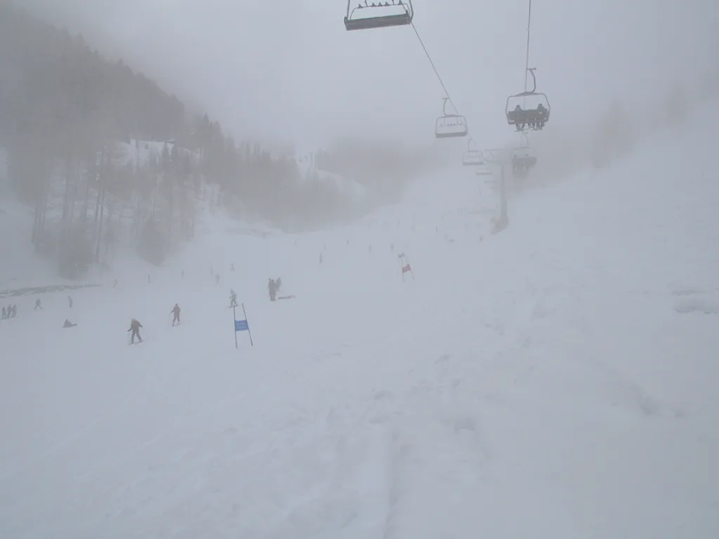 Blick über die neblige Piste mit Sessellift und Rennstrecke.